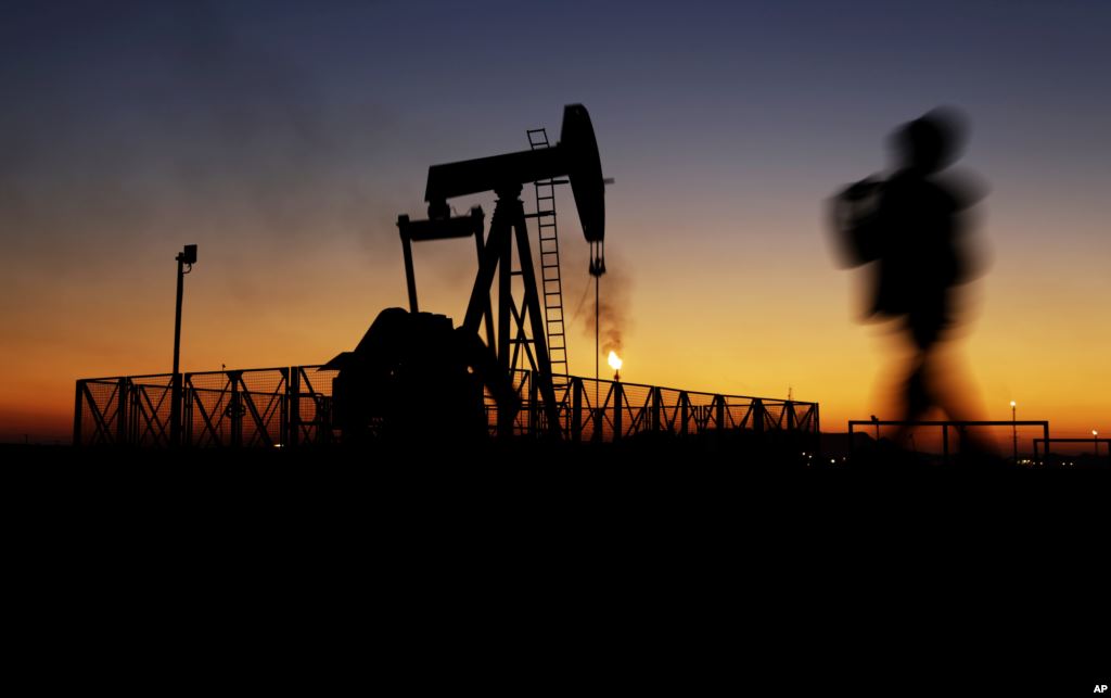 A boy walks by an oil pump at sunset Jan. 18 2016 in the desert oil fields of Sakhir Bahrain