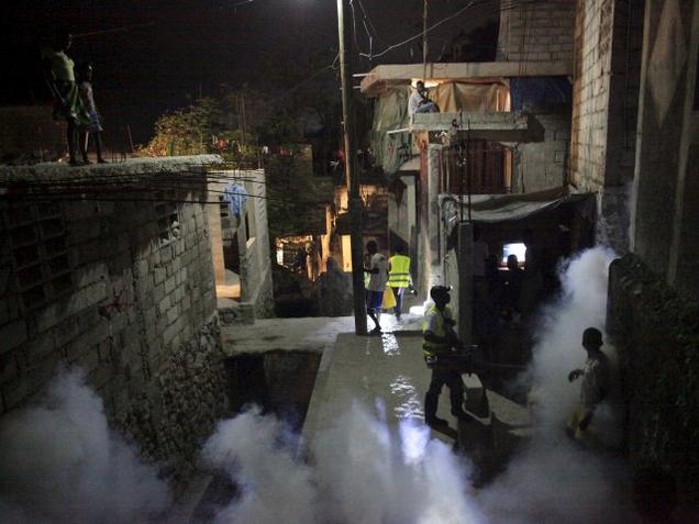 A worker of the Ministry of Public Health and Population fumigates against mosquito breeding as well as to protect against Zika as residents look at him during a regular fumigation campaign carried out together with FOKAL organisation in Martissant Por