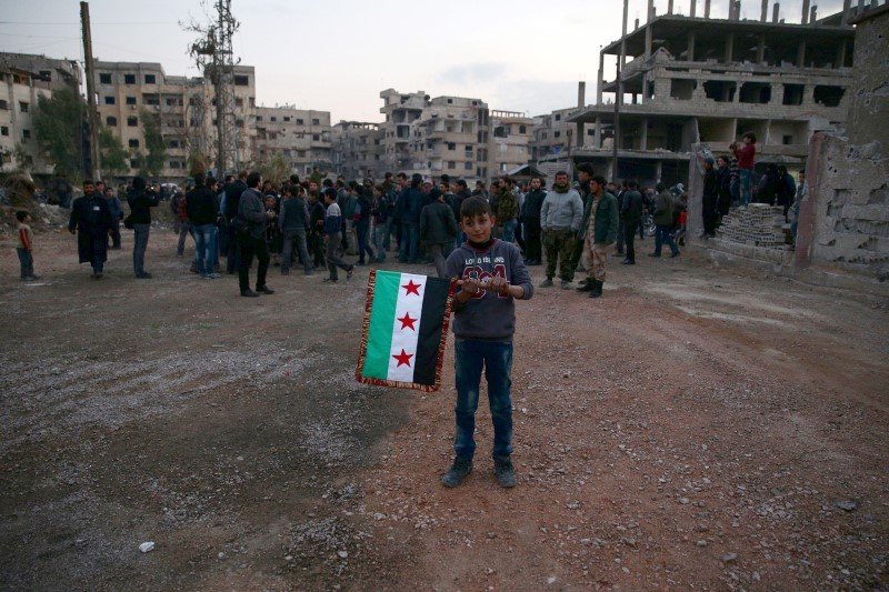 A boy carries an opposition flag as rebel fighters and civilians gather during the arrival of an aid convoy of Syrian Arab Red Crescent and United Nation to the rebel held besieged town of Kafr Batna on the outskirts of Damascus Syria February 23