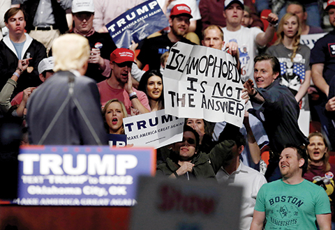 Republican presidential candidate Donald Trump left looks on as a Trump supporter reaches for a sign that reads'Islamophobia is not the answer at a rally in Oklahoma City Friday Feb. 26 2016