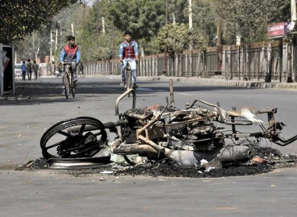 People ride their bicycles close to a damaged motorcycle set alight by protesters during a demonstration by members of Jat community in Rohtak in Haryana India