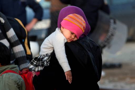 A toddler sleeps while refugees from Afghanistan wait to board a bus as Greek police move them from the Greek Macedonian border near the village of Idomeni