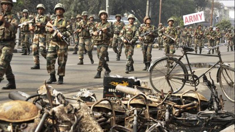 Indian army soldiers conduct a flag march past damaged buildings at Rohtak