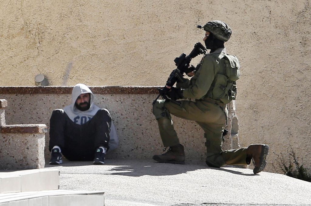 Israeli soldier keeps guard by an arrested Palestinian man at the Amari refugee camp near the West Bank city of Ramallah