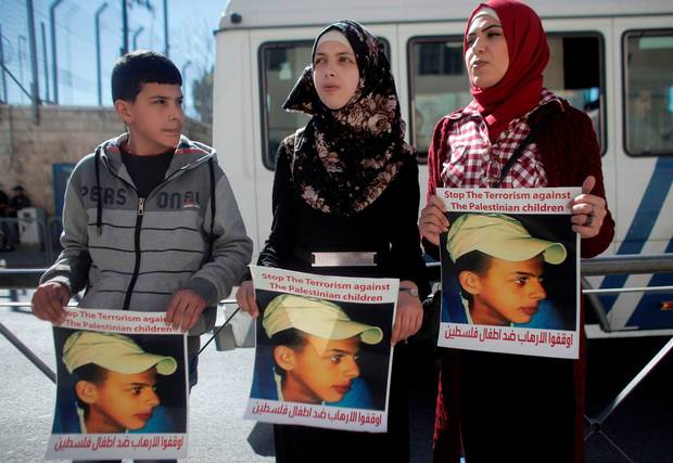 Relatives of Palestinian teenager Mohammed Abu Khdeir who was killed in 2014 hold posters bearing his portrait outside the Jerusalem district court during a hearing