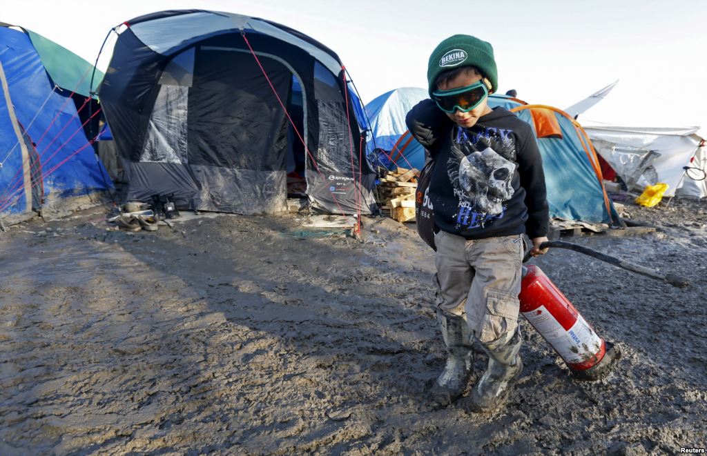 A young migrant pulls a fire extinguisher in a muddy field at a camp of makeshift shelters for migrants and asylum-seekers from Iraq Kurdistan Iran and Syria called the Grande Synthe jungle near Dunkirk France