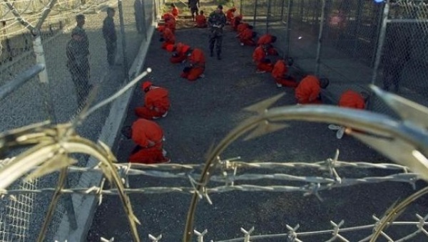 Detainees sit in a holding area under the watch of military police during in-processing to the temporary detention facility at Guantanamo Bay Jan. 11 2002