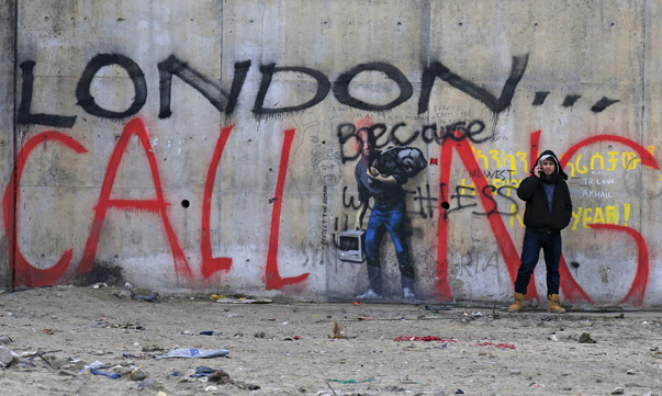 A migrant uses a phone at the camp known as the'Jungle, a squalid sprawling camp in Calais northern France