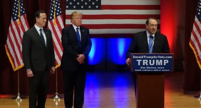 Donald Trump looks on with Rick Santorm as Mike Huckabee speaks during a Trump campaign rally raising funds for US military veterans at Drake University in Des Moines Iowa