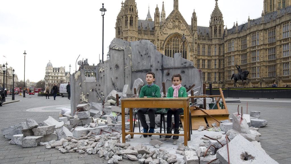 Two children whose school was bombed in Aleppo pose in a mock destroyed classroom — set up by the charity Save the Children — outside the Houses of Parliament in London on Wednesday one day before a donor conference aiming to raise money for victims