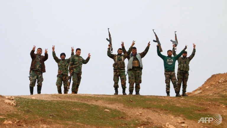 Syrian government forces raise their weapons as they patrol after taking control of the village of Kiffin