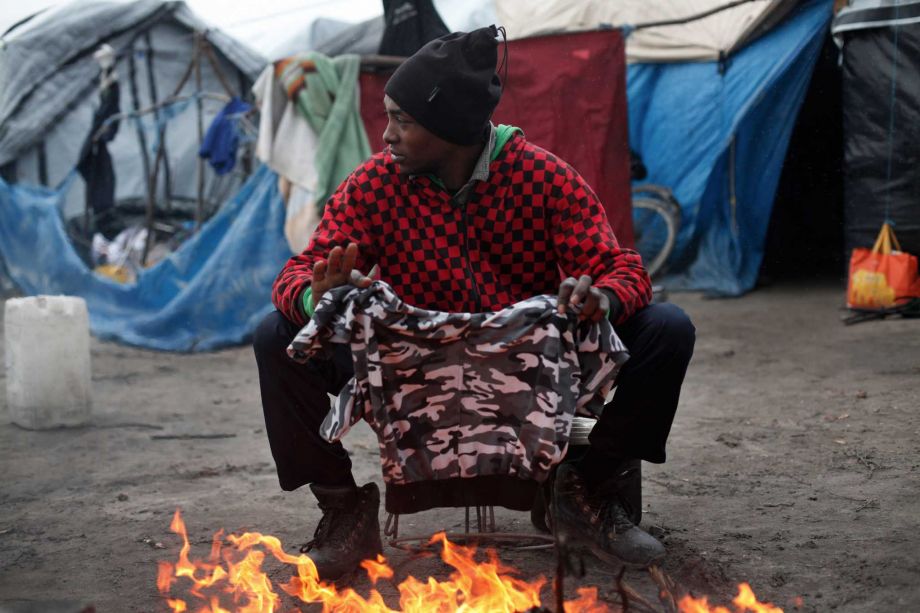 A migrant dries his clothes above a fire in the migrant camp of Calais north of France Thursday Feb. 4 2016. About 4,000 people from Syria Sudan and other countries are estimated to be camped out in Calais as they try to reach Britain some recently