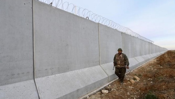 A YPG fighter walks near a wall which activists said was put up by Turkish authorities on the Syria Turkish border in the western countryside of Ras al-Ain Syria