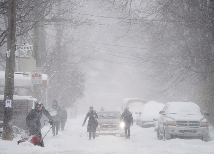 Pedestrians walk in front of traffic as people clear the sidewalk during a snow storm in Toronto on Monday