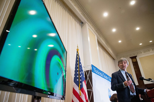 A visual of gravitational waves from two converging black holes is depicted on a monitor as Interferometer Gravitational Wave Observatory Exectutive Director David Reitze speaks during a news conference at the National Press Club in Washington Thu