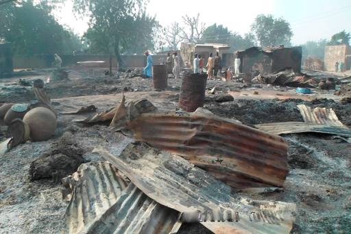 People walk past burnt out houses following an attack by Boko haram in Dalori village 5 kilometers from Maiduguri Nigeria, Sunday Jan. 31 2016. A survivor hidden in a tree says he watched Boko Haram extremists firebomb huts and listened to