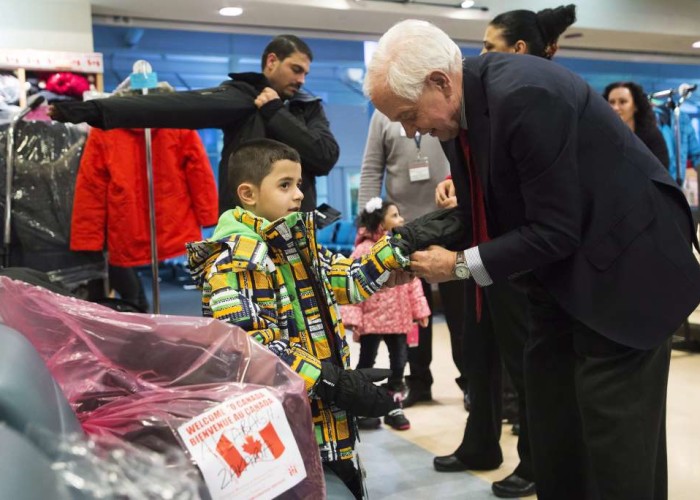 John McCallum right Minister of Immigration Refugees and Citizenship helps Syrian refugee Ramez with his glove at Pearson International Airport in Toronto on Monday