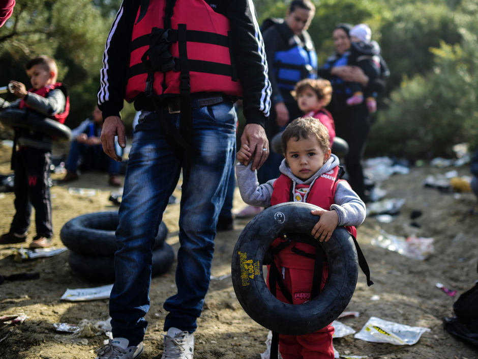 A Syrian child wearing a life-jacket carries a life-belt and holds the hand of an adult before boarding a dinghy to cross the Aegean Sea to the Greek island of Lesbos from the Ayvacik coast in Canakkale on Feb. 28 2016