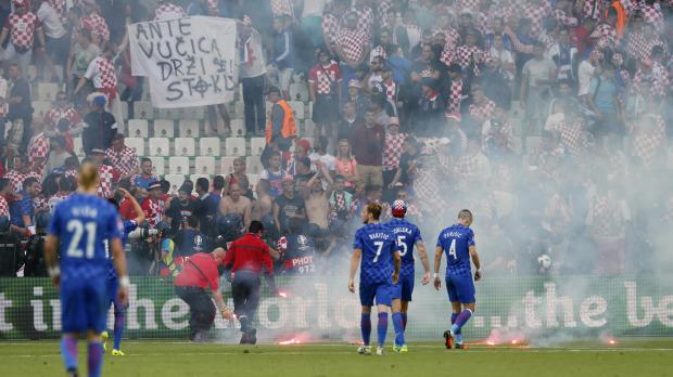 Stewards remove flares from the pitch in front of fans as Croatia players look