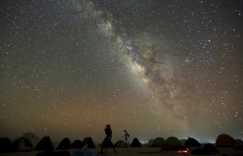 The 'Milky Way&#039 is seen in the night sky around telescopes and camps of people over rocks in the White Desert north of the Farafra Oasis southwest of Cairo