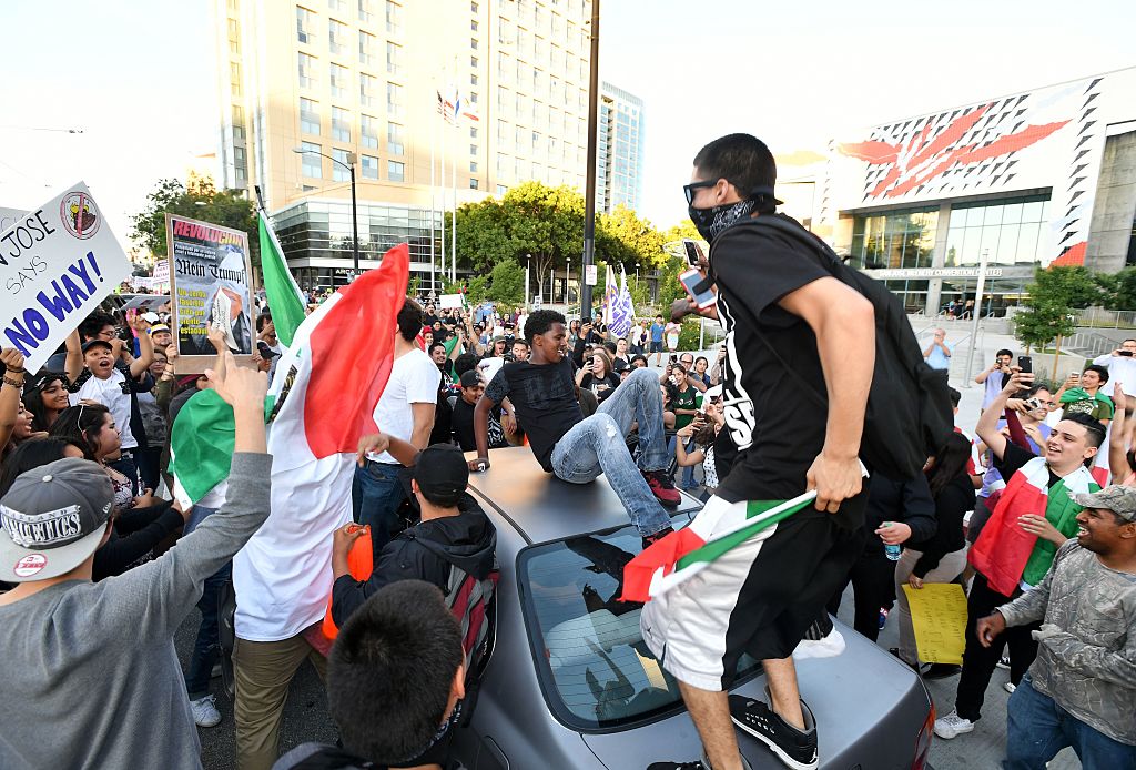 Protesters climb atop a car stopped in traffic as a crowd marches near the venue where Republican presidential candidate Donald Trump was speaking during a rally in San Jose