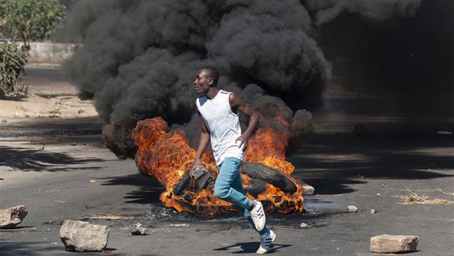 A protester holds a rock next to burning tires during a demonstration in Bulawayo Zimbabwe