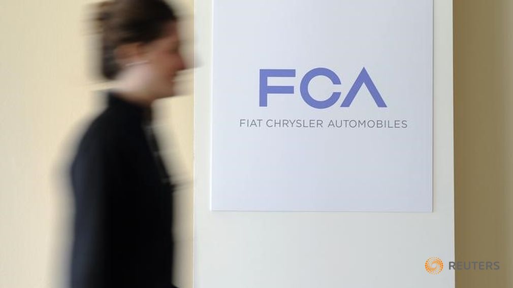 A woman walks past a logo of Fiat Chrysler Automobiles in Turin