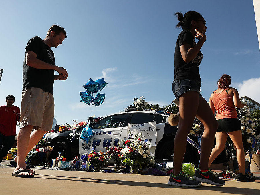 People write condolence notes and lay flowers at a growing memorial in front of the Dallas Police Headquarters near the area that is still an active crime scene in downtown Dallas following the deaths of five police officers last night