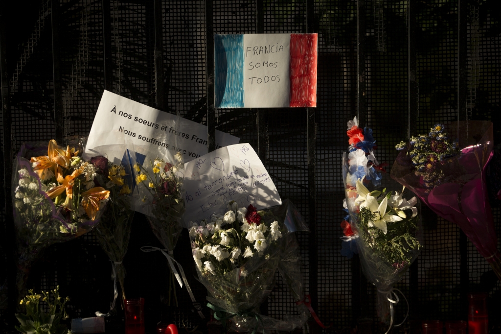 A sheet of paper with the colors of the French flag reading'We are all France in Spanish hangs among flowers outside the French embassy in Madrid Saturday