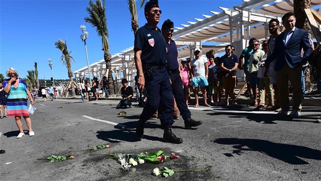 Policemen walk by flowers laid on the ground on la Promenade des Anglais in tribute to the victims of the deadly Bastille Day attack in Nice