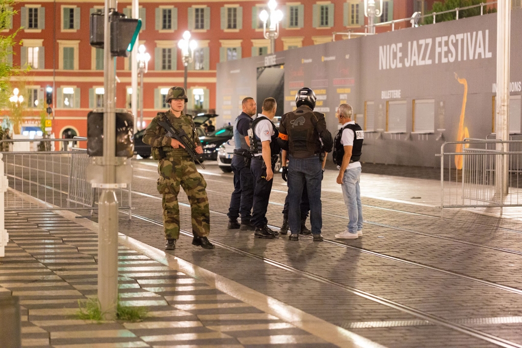 Police officers and a soldier stand by the sealed off area of an attack after a truck drove on to the sidewalk and plowed through a crowd of revelers who'd gathered to watch the fireworks in the French resort city of Nice southern France Friday Ju