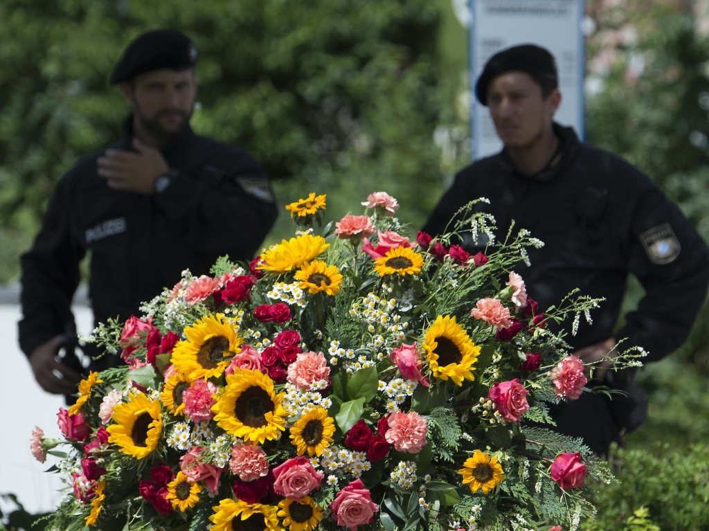 Police officers stand behind a wreath near the Olympia shopping center where a shooting took place leaving nine people dead two days ago in Munich Germany Sunday