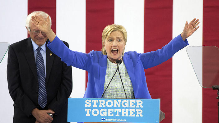 Sen. Bernie Sanders listens as Democratic presidential candidate Hillary Clinton speaks during a rally in Portsmouth