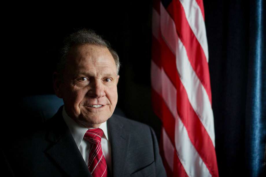 Alabama Chief Justice Roy Moore poses in front the the American flag in Montgomery Ala. Moore has been suspended from office after the Judicial Inquiry Commission accused him of violating the canons of judicial