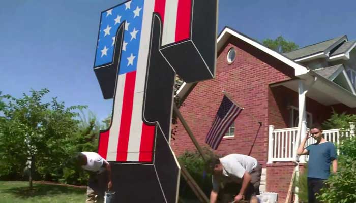 Sign maker Scott Lo Biado takes a bow after resurrecting his creation a giant T- for Trump. The original sign in a homeowner's yard was destroyed by arson