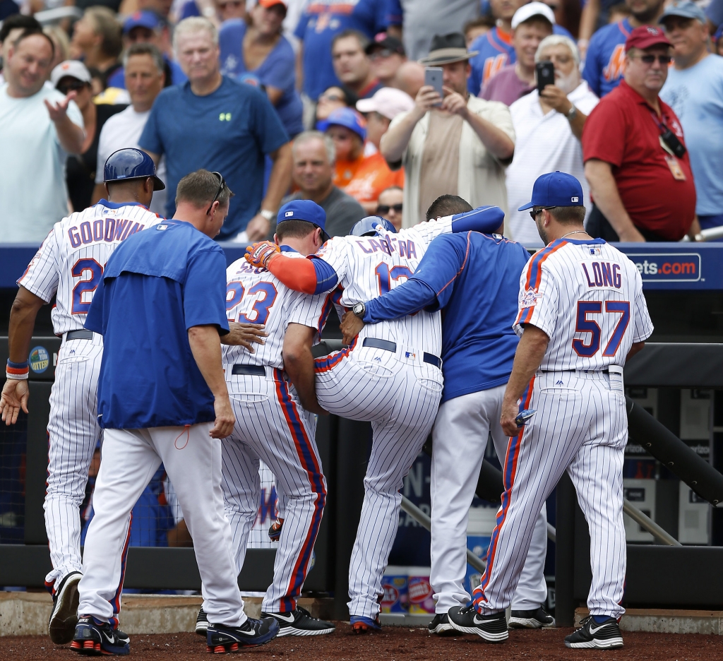 New York Mets first base coach Tom Goodwin left bench coach Dick Scott center and a team trainer second from right help Asdrubal Cabrera off the field after Cabrera doubled over after scoring on Neil Miller ™s first-inning RBI-triple during a bas