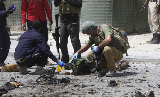 Somali security and a foreign detective check a dead body who was killed in a suicide car bomb attack outside the Criminal Investigation Department in Mogadishu Somalia Sunday