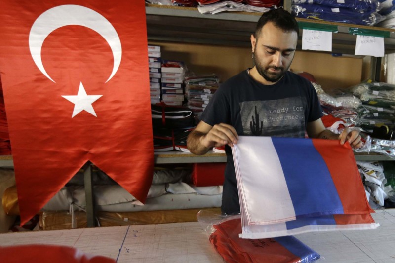 An employee of a flag-making factory folds a Russian flag as a Turkish flag adorns the display at left in Istanbul Tuesday Aug. 9 2016. Turkey's President Recep Tayyip Erdogan arrives in Russia Tuesday for his first overseas trip since the coup