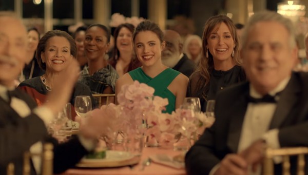 A woman in a green dress sits at a posh dinner looking bored