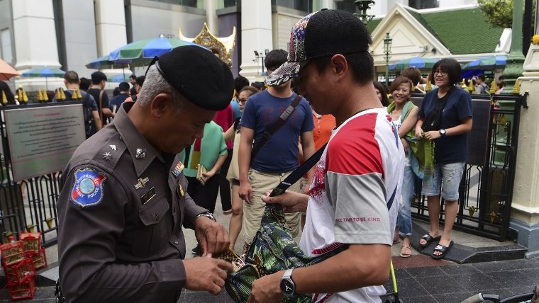 A Thai policeman searches a visitor's bag at in the center of Bangkok as authorities increase security following a string of bomb attacks in Thailand