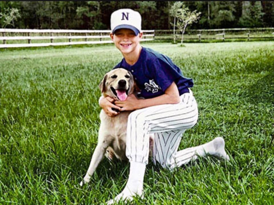 A young Tim Tebow hugs his late dog Otis while wearing his baseball uniform