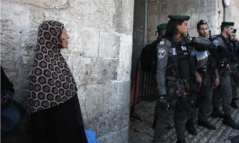 A Palestinian woman looks at Israeli border police guarding the scene of a Palestinian stabbing attack near the Herod's Gate entrance to the Old City of Jerusalem