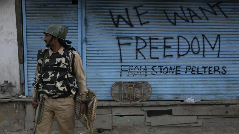 An Indian paramilitary soldier stands near a graffiti on a closed shop in Srinagar Indian controlled Kashmir Sunday