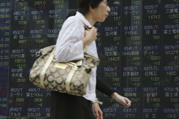 Women walks past an electronic stock board showing