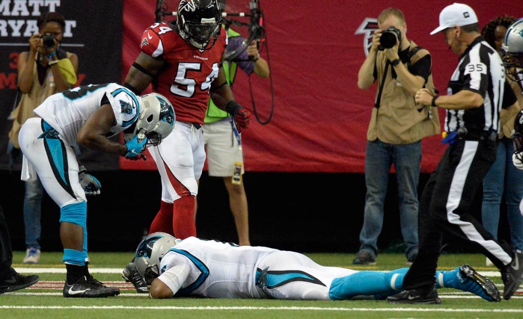 Carolina Panthers quarterback Cam Newton lies on the turf as running back Fozzy Whittaker referee John Hussey, and Atlanta Falcons defensive end O'Brien Schofield look down at him after a hit during a two-point conversion in the second