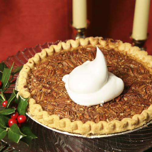 A delicious pecan pie garnished with holly and a dollop of whipped cream