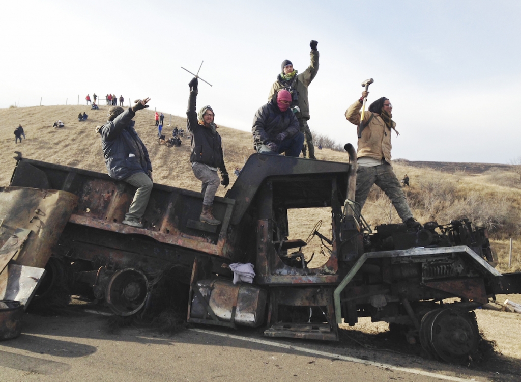 Protesters against the Dakota Access oil pipeline stand on a burned-out truck near Cannon Ball N.D. Monday Nov. 21 2016 that they removed from a long-closed bridge on Sunday on a state highway near their camp in southern North Dakota. Opponents skirm