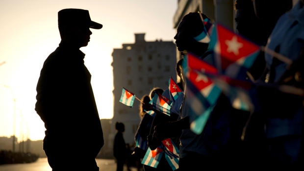 A soldier is silhouetted against the early-morning sky as people holding Cuban flags wait for the motorcade transporting the remains of Cuban leader Fidel Castro in Havana