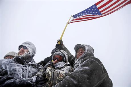 Military veterans huddle together to hold a United States flag against strong winds during a march to a closed bridge outside the Oceti Sakowin camp where people have gathered to protest the Dakota Access oil pipeline in Cannon Ball N.D. Monday Dec. 5