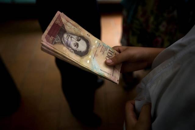 A Venezuelan holds a stack of 100-bolivar bills that have become almost worthless amid the country's hyperinflation